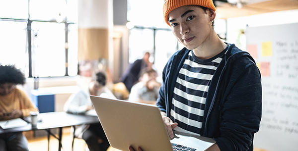 Schler steht mit Laptop im Klassenzimmer